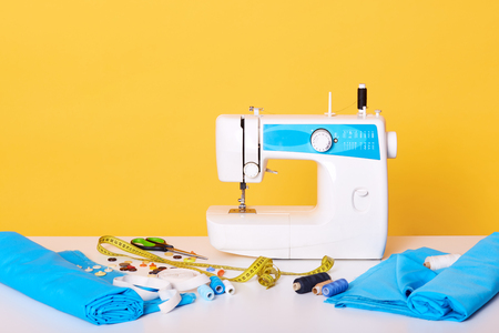 Studio shot of sewing equipments, sewing machine, tap measure, scissors, pieces of cloth, needles, thread isolated over yellow studio background. Image of different tools in sewing workshop,の写真素材