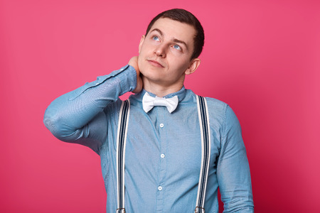 Feeling pain in neck. Frustrated young man in shirt and tie touching his neck and expressing negativity while standing against white backgroundの写真素材