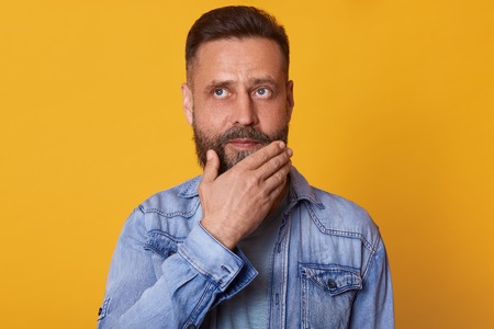 Thoughtful pensive bearded man posing with peaceful facial expression, touching his chin with one hand, looking somewhere up, having lots of new thoughts and ideas. People, life and emotions concept.の写真素材