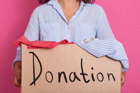 Image of faceless woman wearing blue casual shirt, holding box full of clothes for poor people, box...