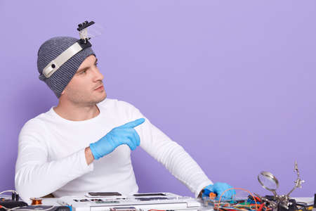 Horizontal picture of young professional electronic engineer fixing laptop, making gesture, looking...