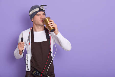 Master of gadget repair service holds phone with black blanck screen for advertisement or promotion, technician wears white shirt and gray cap posing isolated over lilac background. Technology concept.の写真素材