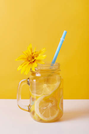 Fresh drink with lemon, glass decorated with yellow flower, summer lemonade with lemon slices and drinking straw, summer non alcoholic cocktail or iced tea for refreshing.の写真素材