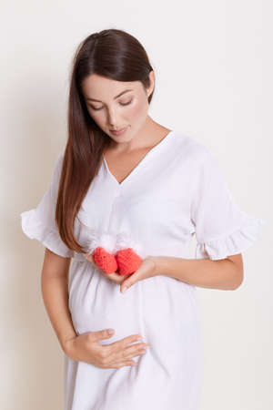 Pregnant woman holding knitted baby booties and looking at it, lady expecting new life, posing...