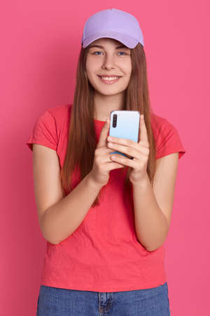 Portrait of attractive pretty cheerful lady holding in hands cell phone, playing game via smart phone while having free time, isolated over bright rosy background.の写真素材