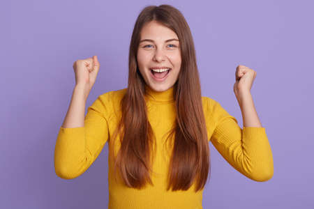Successful female student looks happy, clenches fists, accomplishes goal, exclaims finally victory,...