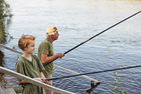 Happy father and son together fishing from wooden stairs, look concentrated, enjoying to spend time together, wants to catch lots fish, family wearing similar t shirt.の写真素材