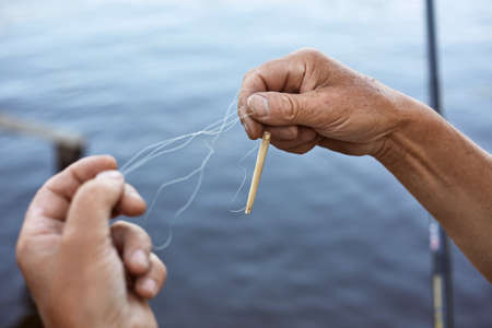 Faceless male untangles knot of fishing line over water on background, unknown person holding...