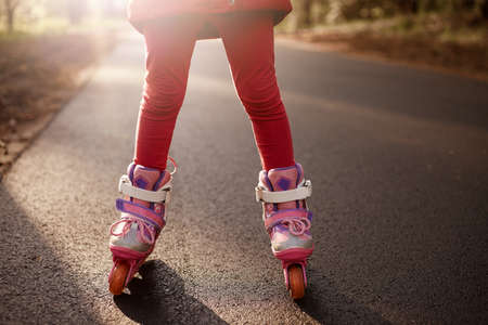 Faceless portrait of little child wearing red leggins and pink rolling skate, posing on asphalt...