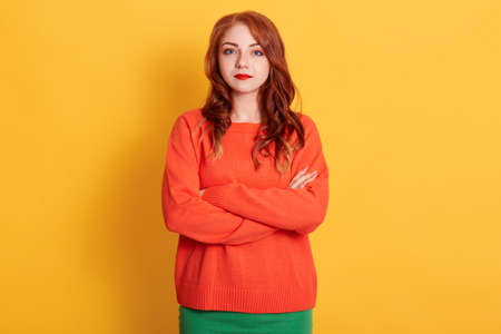 Portrait of young tender red haired european woman with serious look, wearing orange sweater,...