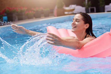 Happy young woman in bikini with rubber inflatable mattress, playing and having good time at water...