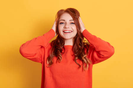 Surprised happy woman wearing warm orange sweater posing isolated over yellow background, looks at...