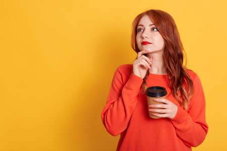 Woman thinking about future, holding disposable cup of coffee, looking aside, wearing casually, copy space for advertisement or promotional text, red haired female with pensive look.の写真素材