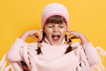 Dark haired baby covered her ears with finger, child does not want to hear anything, young female...