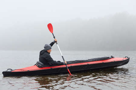 Profile of man floating on lake in kayak, looking concentrated on his way, rowing boat in cold cloudy day, water sport, guy in black jacket padding, pastime in active way.の写真素材