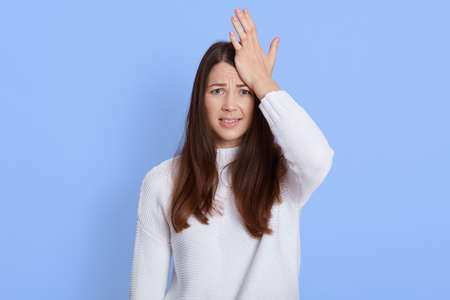 Frustrated forgetful young woman looking at camera with worried expression, holding palm on head,...