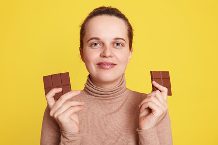 Pregnant woman holding two bars of chocolate in both hands and looking directly at camera with...