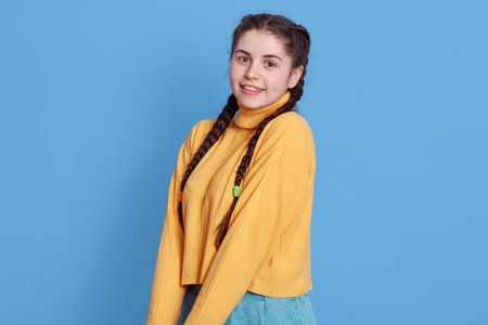 Smiling Caucasian woman keeping hands together and looking directly at camera, attractive brunette female wearing yellow sweater standing isolated over blue background.の写真素材