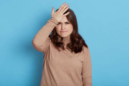 Disappointed woman keeps palm on forehead, regrets, did something wrong, having problematic...