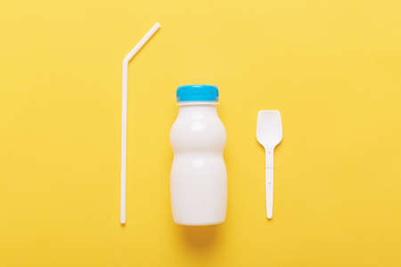 Three subjects isolated over yellow background, bottle from milk or yogurt, plastic spoon and straw,...