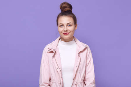 Portrait of young happy woman looking smiling directly at camera isolated lilac background, wearing pale pink jacket and white shirt, has hair bun, lady with pleasant appearance.の写真素材