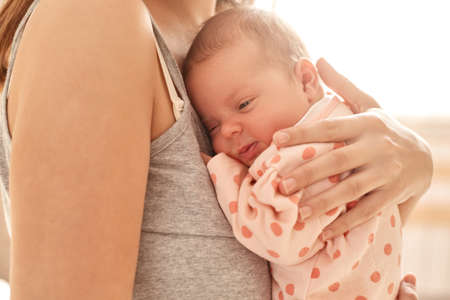 Mother holding newborn baby girl on light background, faceless female dresses casual sleeveless t shirt hugging her infant and express love, tiny baby with mommy.の写真素材