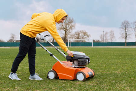 Man cutting green grass with lawn mower in backyard. Gardening country lifestyle. Beautiful view on fresh green grass lawn, landscape in spring or summer seasonの写真素材