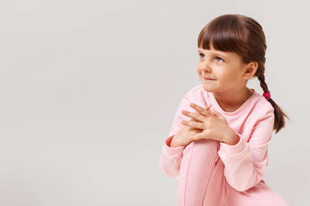 Beautiful cute little girl looks to the side with interest, dressed in pink clothes, has dark hair and two pigtails, copy space for advertisement, isolated over white background.の写真素材