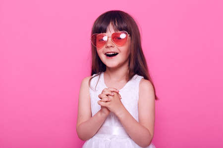 Little girl wearing sun glasses posing on pink background.の写真素材