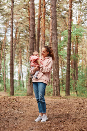 Full length portrait of young adult woman with infant girl in hands, mother with little daughter walking in forest, enjoying fresh air and nature, motherhood, childhood.の写真素材