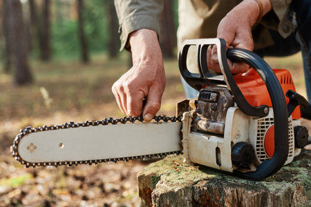 Faceless logger preparing chainsaw for work, cheking saw for faults, unknown logger forester with professional tool for cutting trees on background of forest.の写真素材