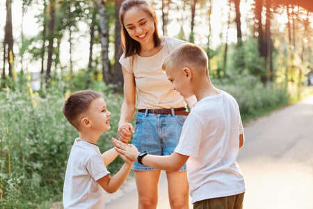 Family having fun while walking in summer park and laughing, little boy gives a high five to his elder brother, happy children standing near their smiling mother.の写真素材