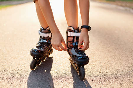 Close-up of an anonymous kid's hands fixing laces on roller blades before skating, unknown child on...