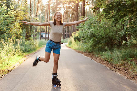 Full length portrait of attractive slim woman wearing casual style attire riding roller skates,...