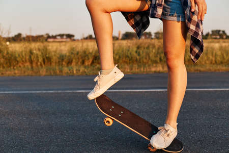 Unknown female person with long beautiful legs wearing white sneakers riding skateboard, faceless...