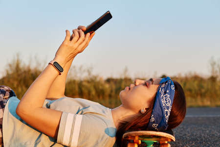 Side view portrait of slim beautiful woman wearing hair band and t shirt laying on asphalt road and...