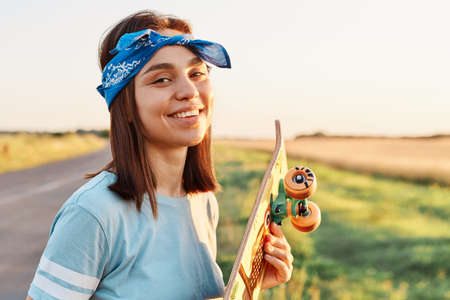 Outdoor shot of young adult winsome woman wearing blue casual style t shirt and hairband, standing...