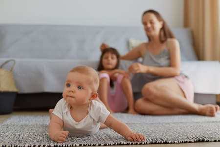 Closeup portrait of crawling baby boy or girl, mother and elder daughter posing on background, having fun and spending time together, people posing at home in light room.の写真素材