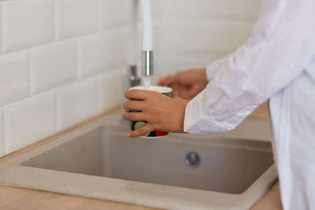 Human hand holding cup pouring fresh water at kitchen faucet, wants to drink fresh water or washing...