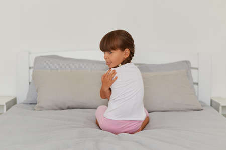Indoor shot of offended female kid sitting on the bed, turning to camera and showing tongue out, felling sadness, sad lonely kid being bullied abused.の写真素材