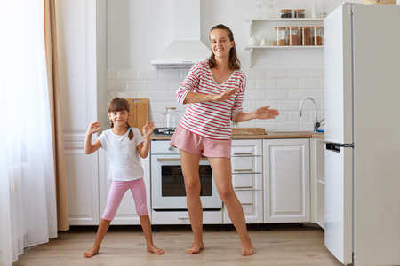 Full length portrait of happy mother feeling amazing dancing with her loving daughter, looking at camera, expressing optimistic emotions, having fun together.の写真素材