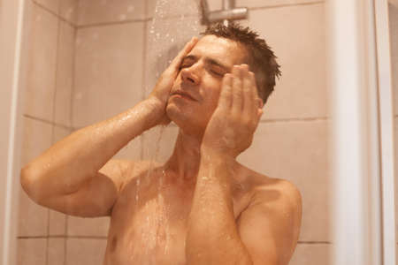 Portrait of handsome young man taking shower, standing under hot water, washing his face, posing naked, keeping eyes closed, refreshment after hard working day.の写真素材