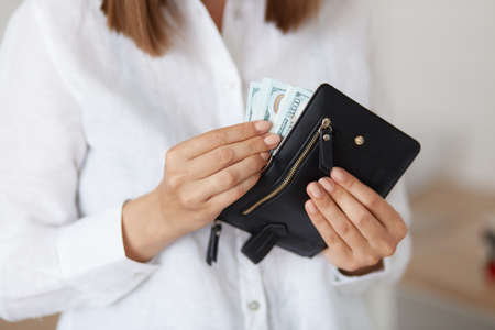 Indoor shot of unknown female wearing white casual style shirt holding black leather wallet with...