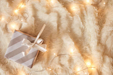 Top view of gray wrapped present box on white soft blanket decorated with garland lights, copy space for promotion. Merry Christmas and happy new year.の写真素材