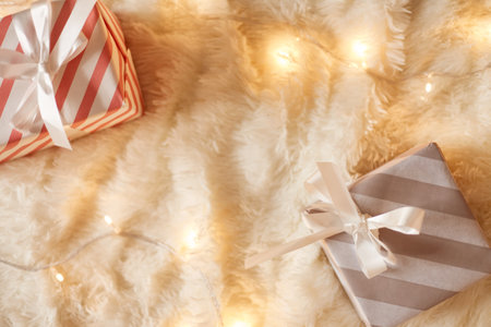 Top view of wrapped gift boxes on white soft blanket decorated with garland lights, copy space for advertisement or promotional text. Merry Christmas and happy new year.の写真素材