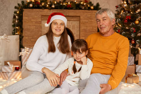 Portrait of happy family, mature man wearing orange sweater, his daughter and granddaughter sitting...