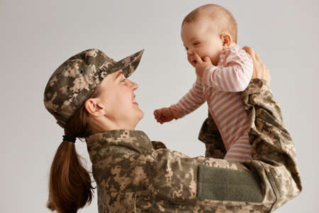 Portrait of female soldier just arrived home and being so happy to see her infant daughter, lifting toddler and looking at baby with great love and smile.の写真素材