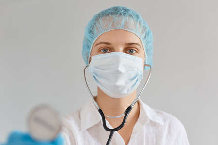 Portrait of attractive Caucasian female doctor wearing medical uniform, cap and surgical mask...