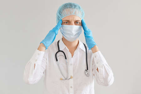 portrait of unhealthy woman doctor wearing medical cap, gloves and protective mask, standing with...