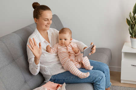 Indoor shot of happy mom and cute kid baby using smartphone for broadcasting livestream or having...